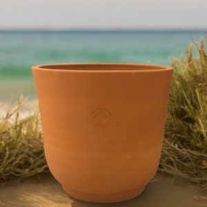cup shaped red terra cotta planter on beach with water in background