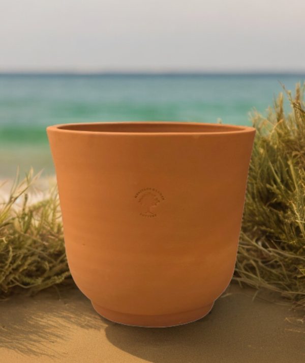 cup shaped red terra cotta planter on beach with water in background