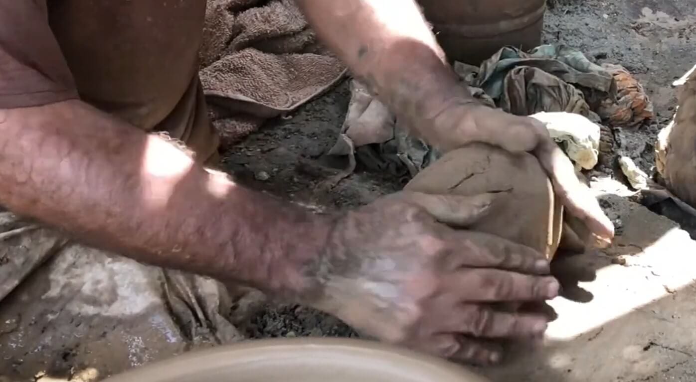 Artisan kneading and wedging raw Indus River clay to prepare it for throwing