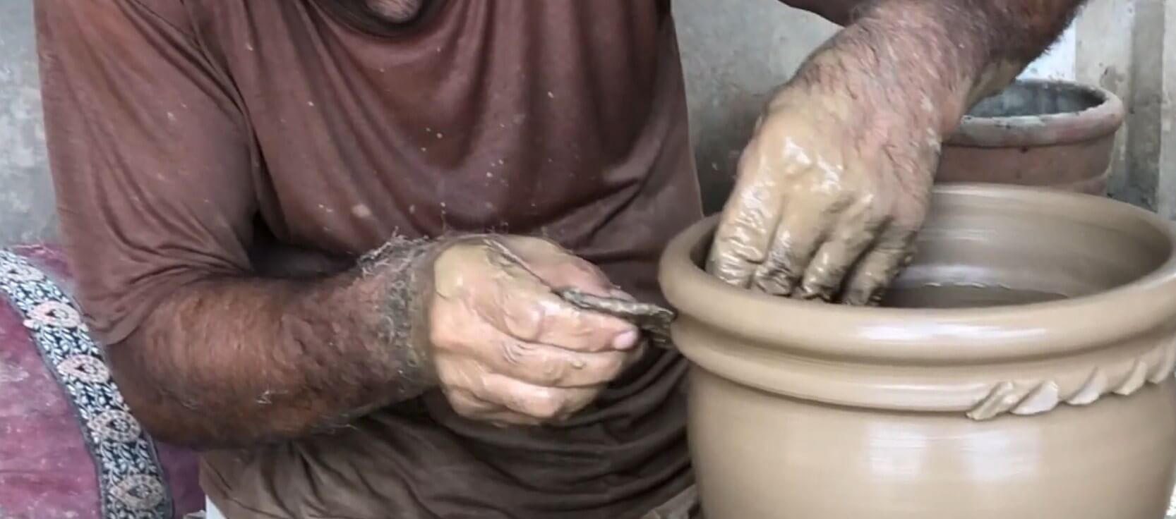 Artisan carving decorative patterns into a leather-hard terracotta pot