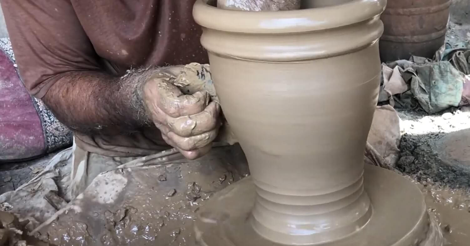 Artisan shaping and refining a terracotta pot using wooden ribs and tools