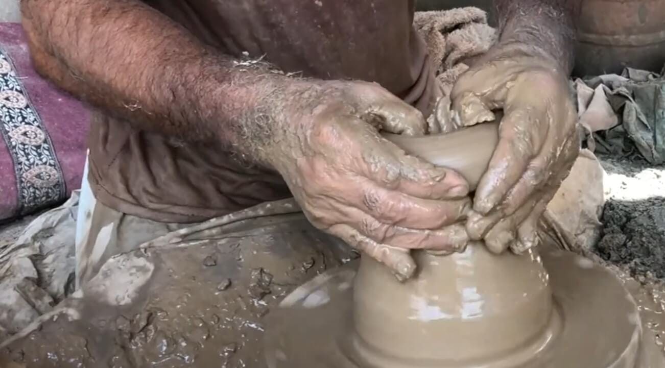 Close-up of an artisan's hands pulling up clay walls on a spinning wheel